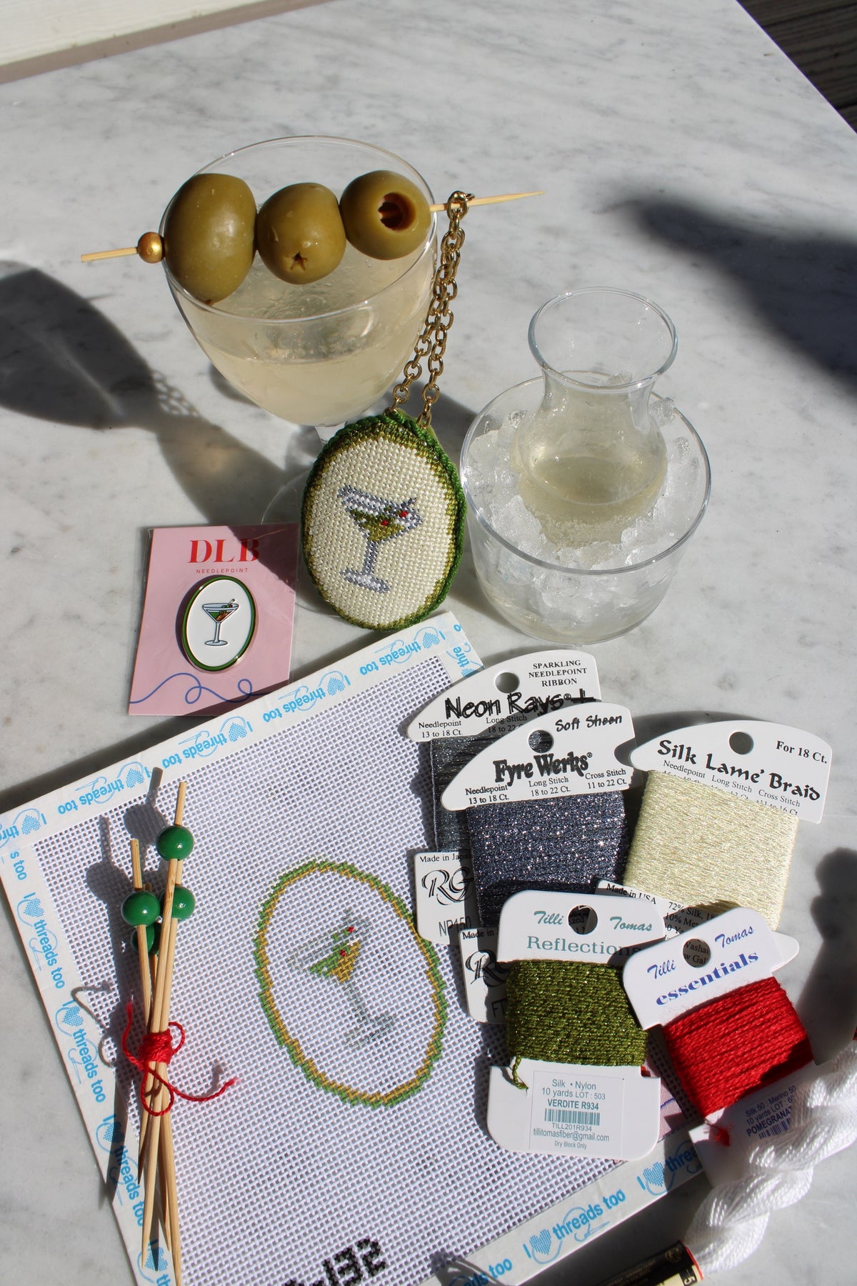One month's Cocktail Club kit: the Dirty Martini ornament canvas on 13 mesh with its threads, cocktail picks, a DLB martini needle minder and the finished ornament